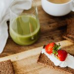 Start your day with a nutritious breakfast featuring rye toast with cream cheese and strawberries, paired with green juice and coffee.